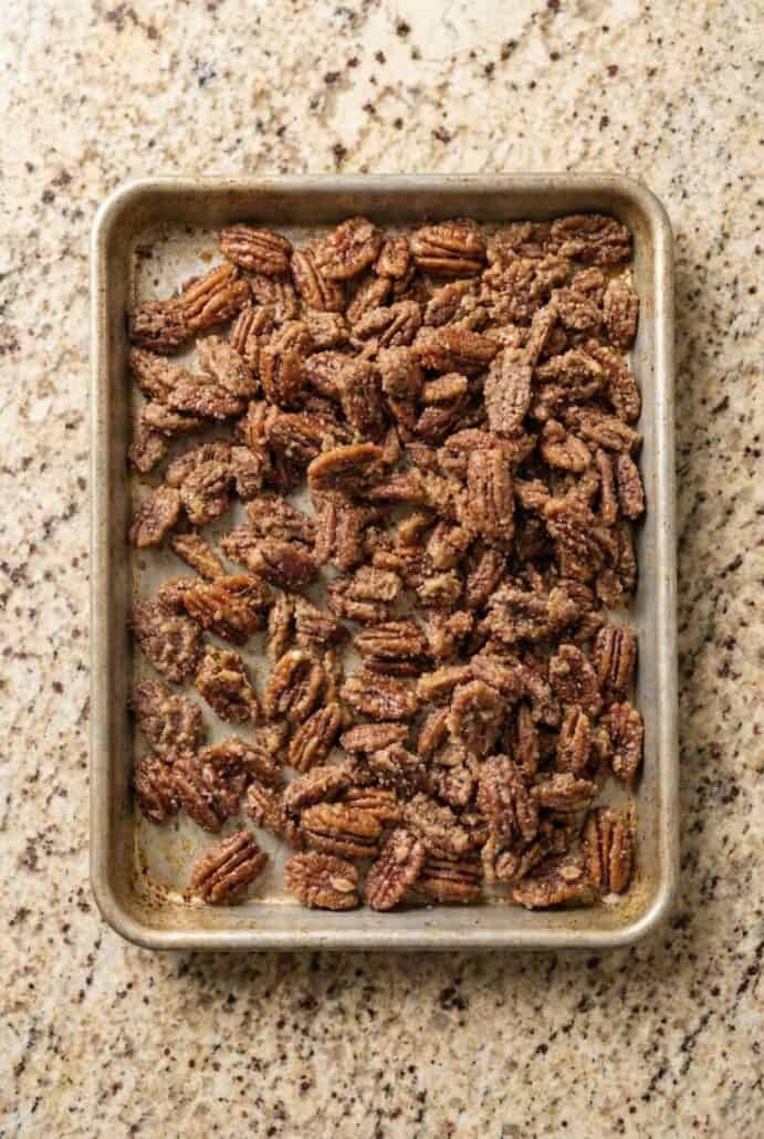 Overhead view of oven roasted cinnamon glazed pecans on a baking sheet, showing the crisp sugary coating forming during the Texas candied pecans recipe.