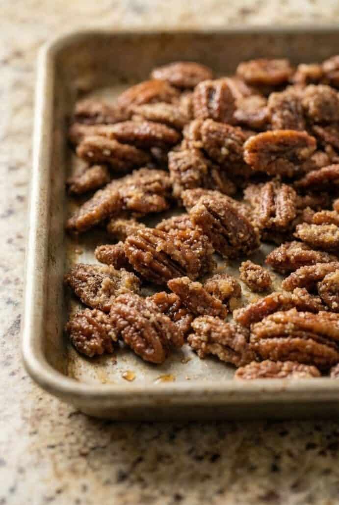 Close-up of freshly baked cinnamon sugar pecans on a sheet pan, highlighting the crisp glazed coating.