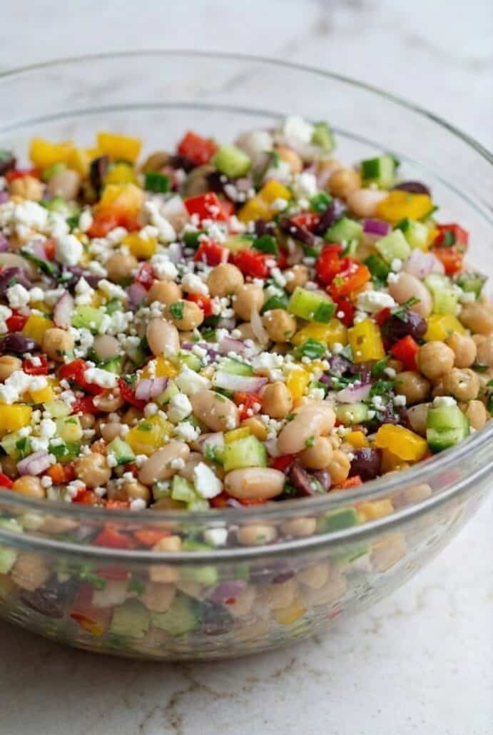 TikTok Dense Bean Salad in a clear glass bowl, filled with chickpeas, cannellini beans, diced vegetables, and crumbled feta cheese.