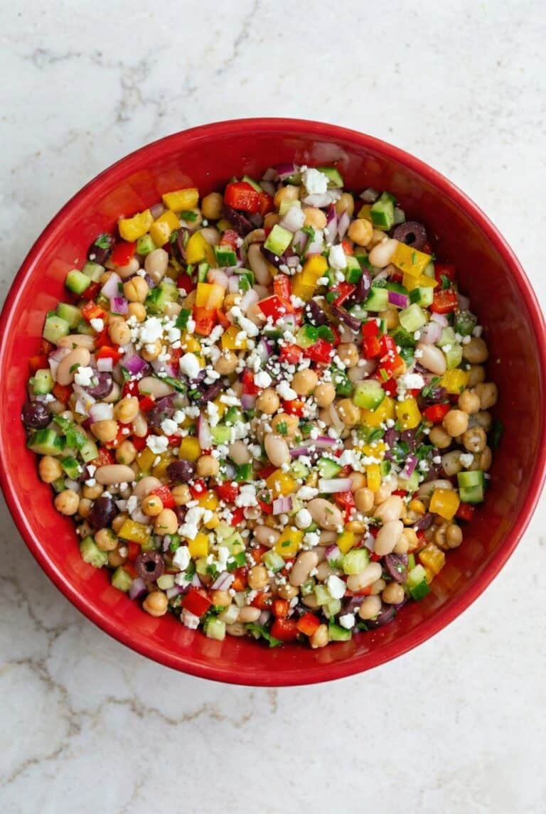 Colorful TikTok Dense Bean Salad in a red bowl, filled with chickpeas, white beans, chopped vegetables, olives, and crumbled feta.