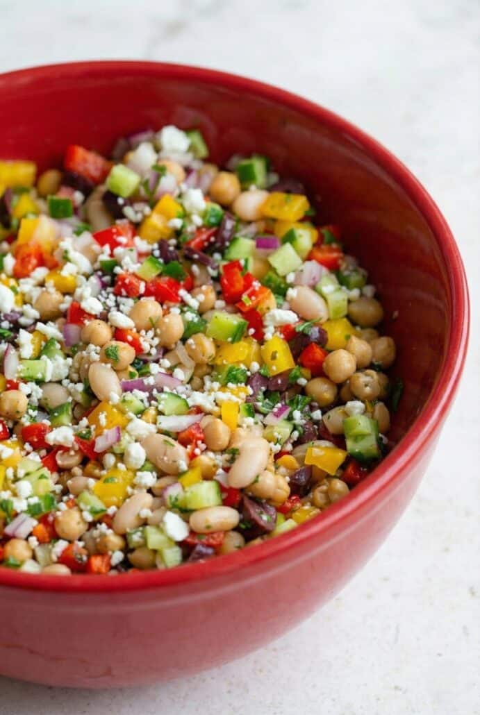 Close-up of colorful TikTok Dense Bean Salad in a red bowl, featuring chickpeas, white beans, bell peppers, cucumbers, and crumbled feta.