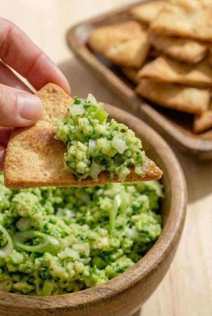 A hand scooping TikTok Green Goddess Salad onto a crispy pita chip, highlighting the popular viral salad’s creamy texture and dip-worthy appeal.
