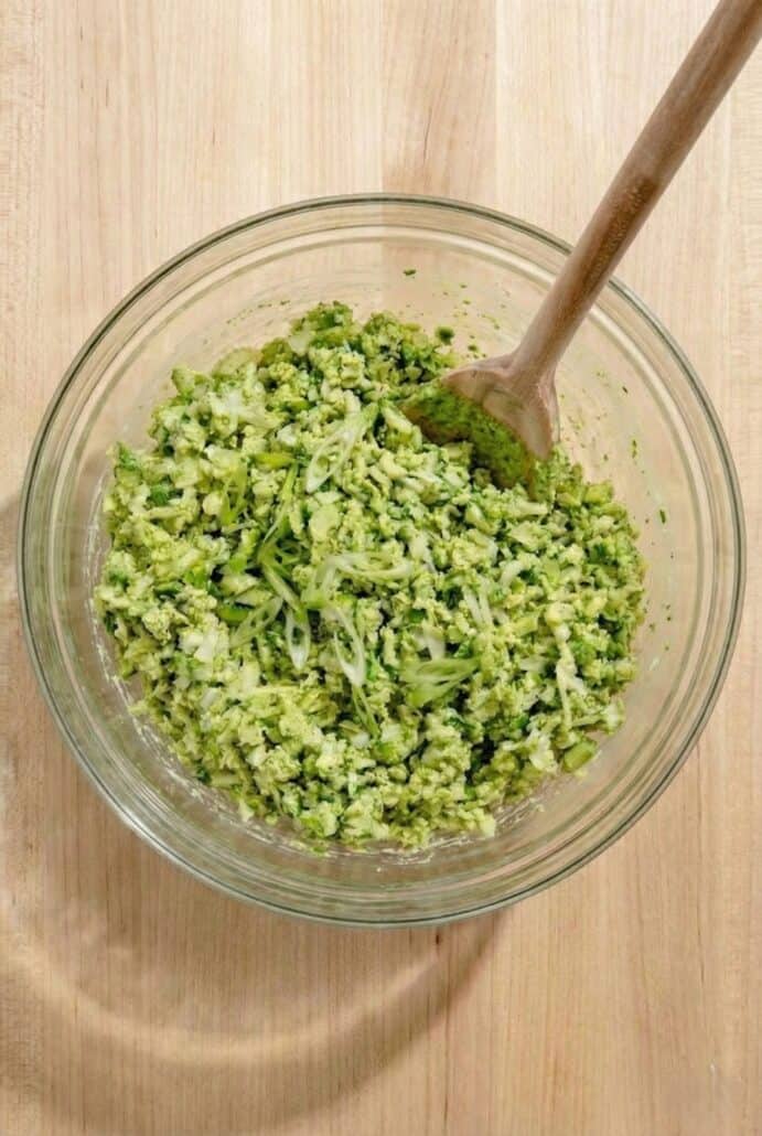 A glass bowl filled with freshly mixed TikTok Green Goddess Salad, featuring finely chopped green vegetables coated in creamy herb dressing.