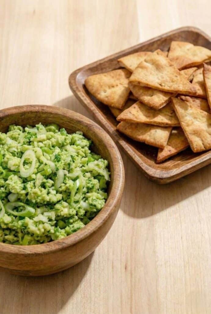 A serving of TikTok Green Goddess Salad in a wooden bowl next to crispy pita chips.