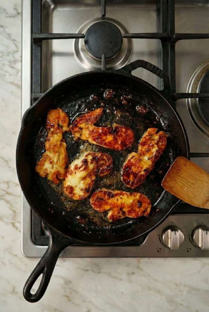 Halloumi slices sizzling in a cast iron skillet on the stovetop.