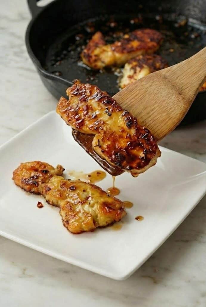 Golden brown halloumi being plated from a cast iron skillet with a wooden spatula.
