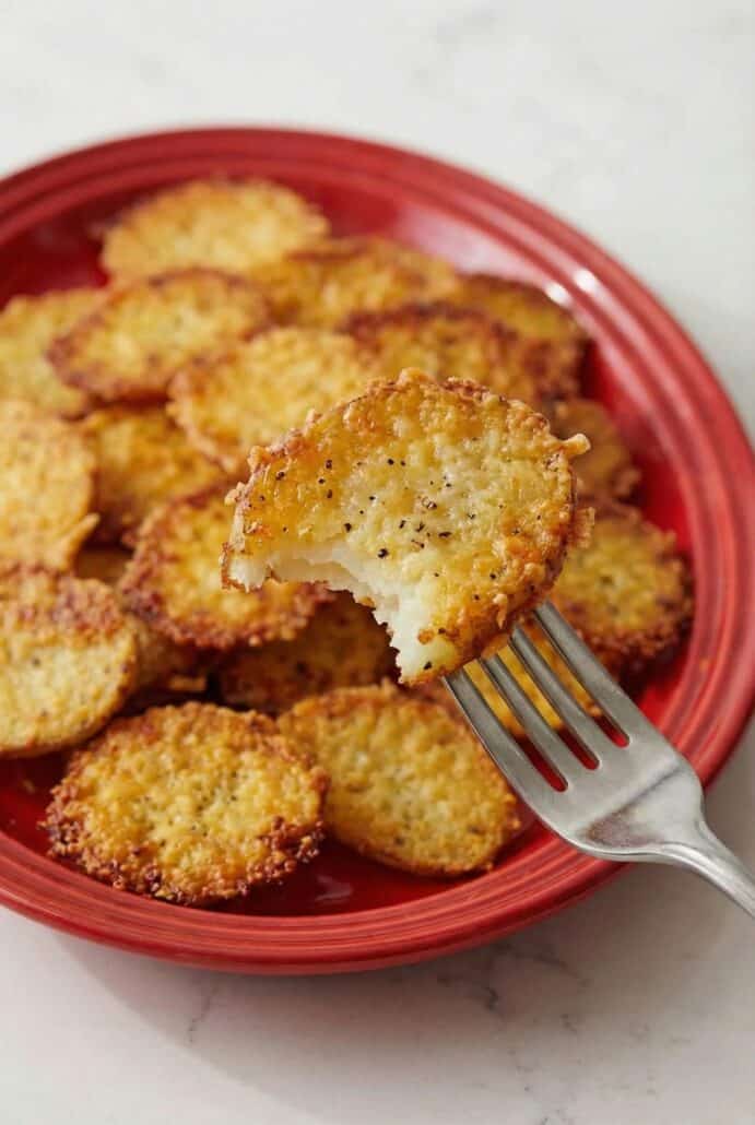 Close-up of a crispy Parmesan crusted roasted potato with a bite taken out, showing the creamy inside.