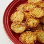 Crispy parmesan crusted roasted potatoes served on a red plate. A delicious and golden appetizer.