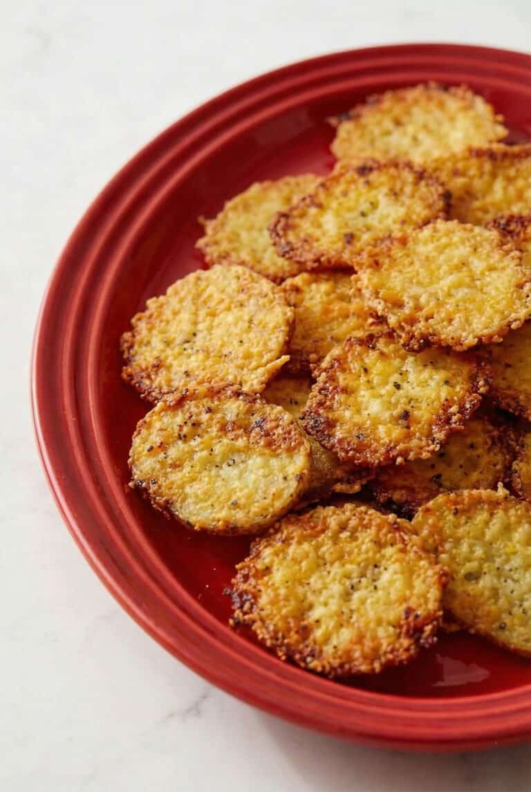 Crispy parmesan crusted roasted potatoes served on a red plate. A delicious and golden appetizer.