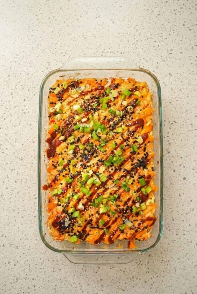 Overhead view of a fully baked TikTok Salmon Sushi Bake in a glass casserole dish, topped with spicy mayo, furikake, and green onions, ready to serve.