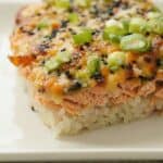Close-up of a baked salmon sushi casserole topped with green onions and furikake, served on a white plate.