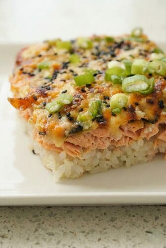 Easy Creamy Salmon Sushi Bake TikTok Recipe Close-up of a baked salmon sushi casserole topped with green onions and furikake, served on a white plate.