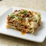 Slice of viral dumpling lasagna layered with dumpling wrappers and savory chicken filling, topped with sesame sauce and chili oil.