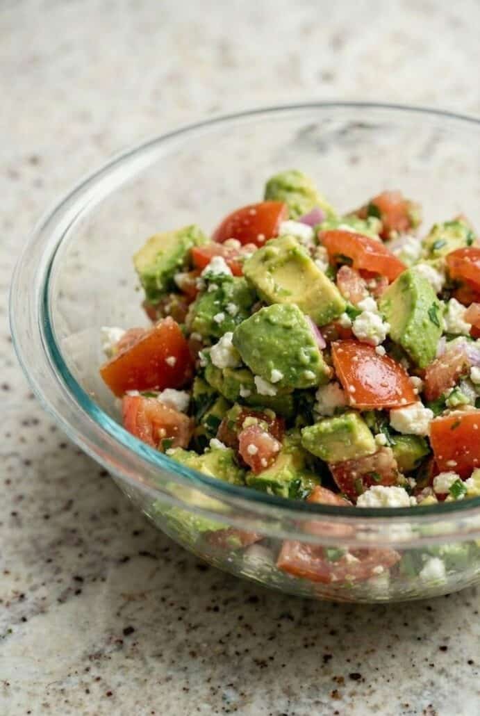 Glass bowl filled with fresh avocado feta salsa made with chopped avocado, tomatoes, herbs, and feta cheese.
