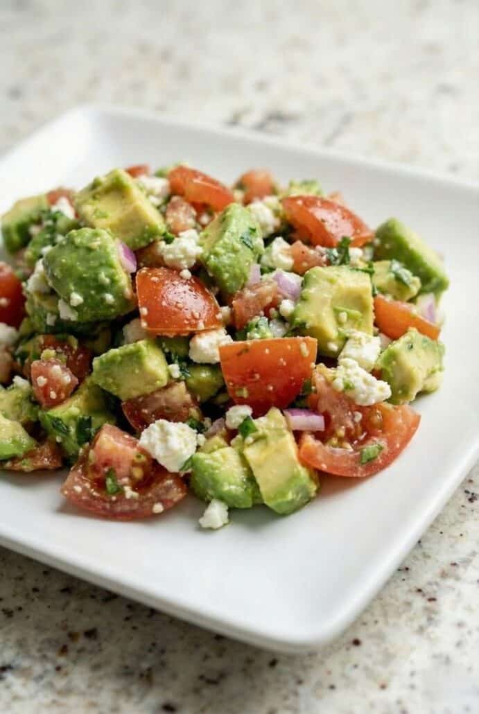 Close-up of chunky avocado feta salsa with diced tomatoes, avocado, herbs, and crumbled feta served on a white plate.