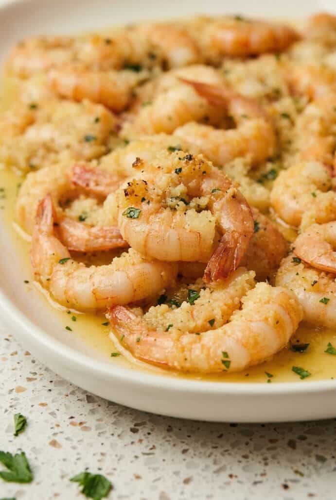 Close-up of baked shrimp scampi on a plate, showcasing tender shrimp in garlic butter sauce, topped with fresh herbs.