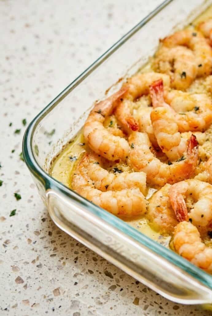 Close-up of shrimp scampi in a glass baking dish with garlic butter sauce, showcasing tender shrimp and fresh herbs.