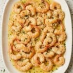 A plate of baked shrimp scampi in garlic butter sauce, topped with a sprinkle of fresh parsley.