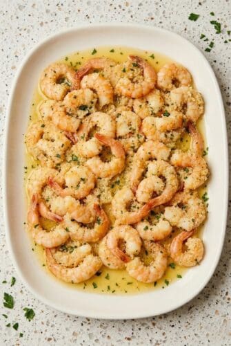 A plate of baked shrimp scampi in garlic butter sauce, topped with a sprinkle of fresh parsley.