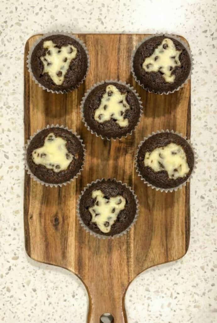 A wooden tray with six freshly baked Black Bottom Cupcakes, each with a creamy, chocolate chip-filled center.