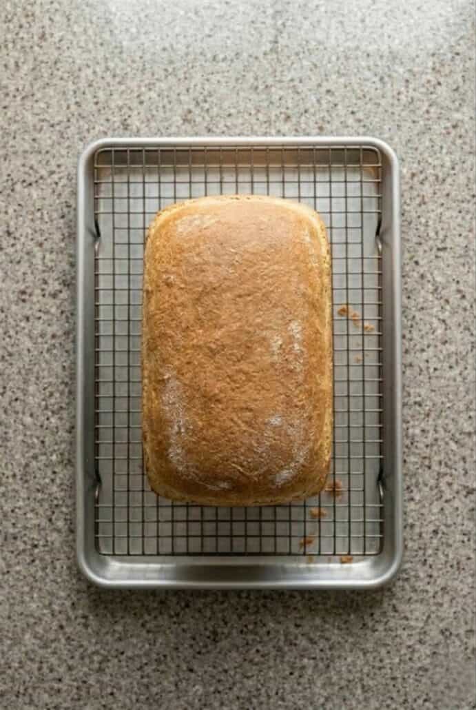 Freshly baked loaf of bread cooling on a wire rack, with a golden-brown crust and perfectly shaped form.