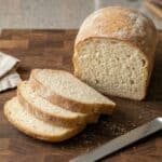 Freshly baked loaf of bread with three slices cut, showcasing a soft and airy texture.