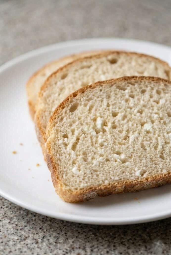 Close-up of three slices of soft, homemade bread on a plate, highlighting its light, airy texture and freshly baked quality.