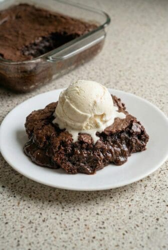 Brownie Pudding | Easy Fudgy Chocolate Dessert Recipe A warm, fudgy chocolate brownie pudding served on a white plate and topped with a large scoop of melting vanilla ice cream.
