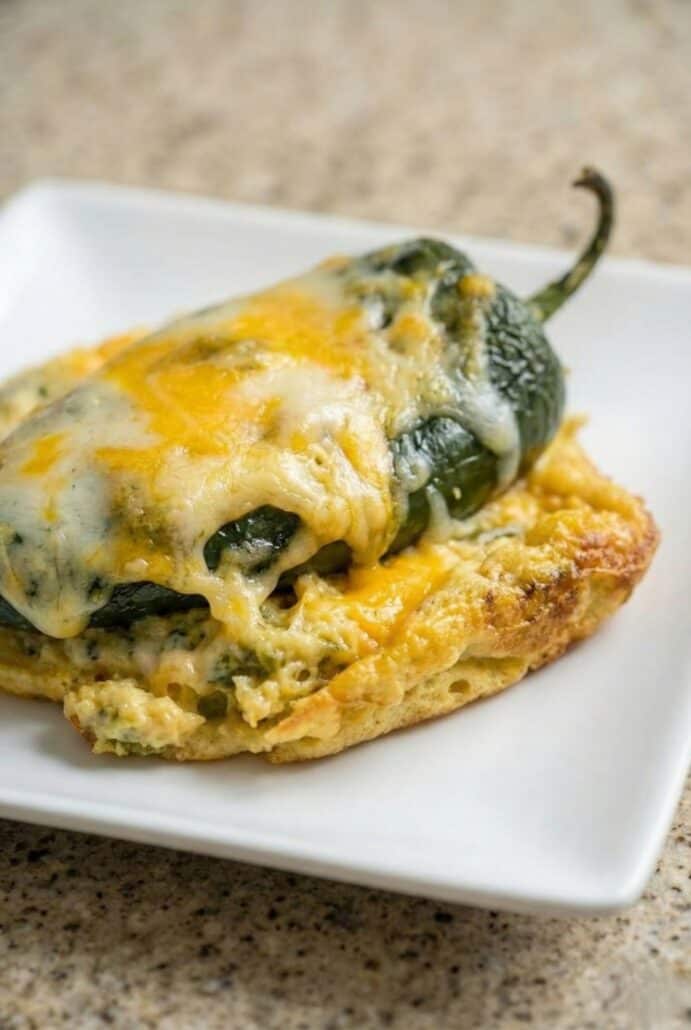 Slice of cheesy chili relleno casserole with roasted poblano peppers and melted cheese served on a white plate from this easy baked casserole recipe.