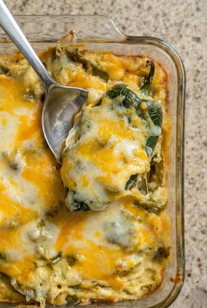 Spoon lifting a serving of cheesy chili relleno casserole with poblano peppers from a baked casserole dish.