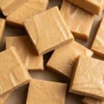 Close-up of creamy peanut butter fudge squares stacked on parchment paper.