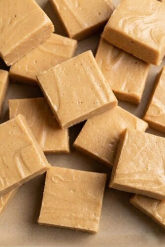 Creamy Peanut Butter Fudge That Melts in Your Mouth – So Easy to Make Close-up of creamy peanut butter fudge squares stacked on parchment paper.