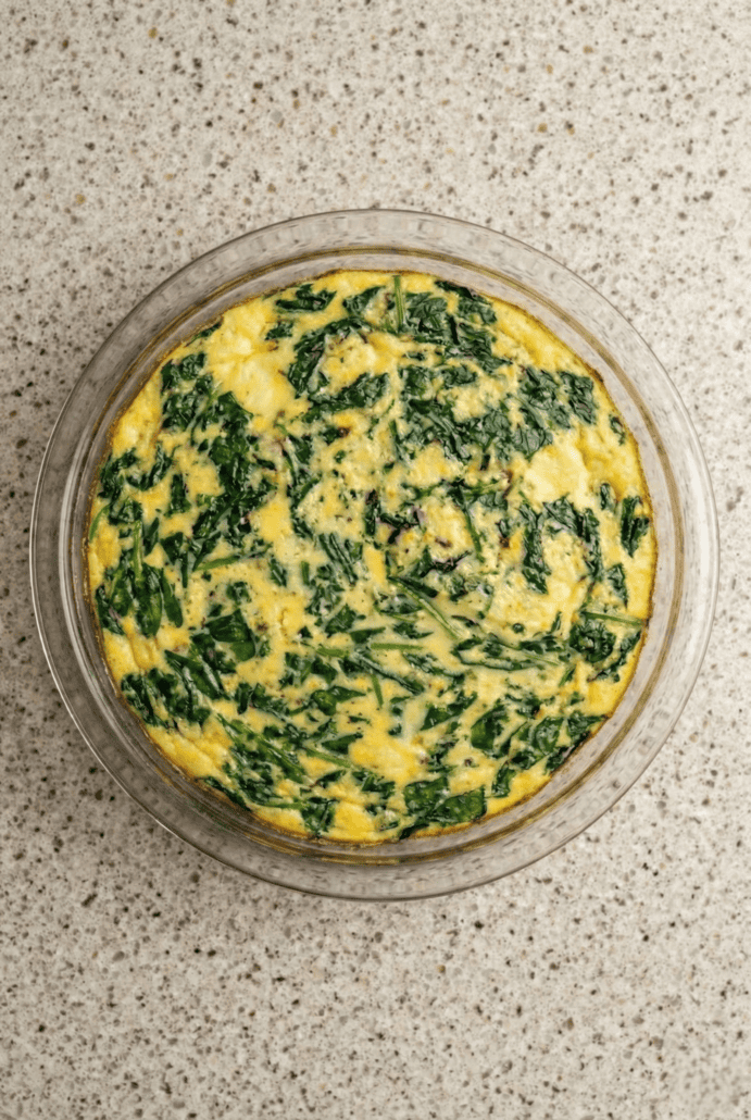 A freshly baked crustless spinach quiche in a glass pie dish, with a vibrant green spinach filling swirled through a golden egg base.