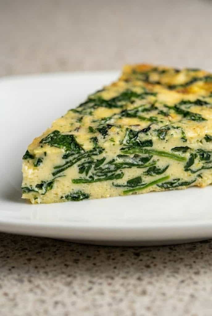 A slice of crustless spinach quiche on a white plate, showcasing the vibrant green spinach mixed with fluffy eggs.
