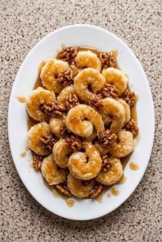 Honey walnut shrimp coated in creamy sauce and topped with candied walnuts, served on a white platter.