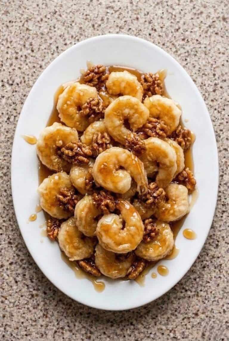 Honey walnut shrimp coated in creamy sauce and topped with candied walnuts, served on a white platter.