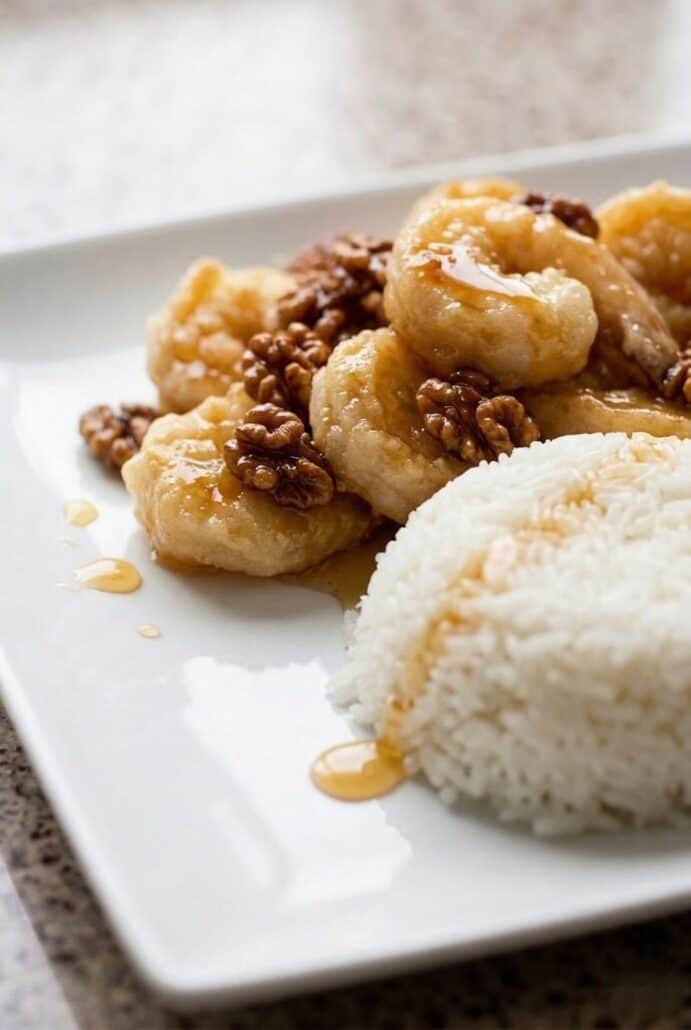 Honey walnut shrimp served with white rice on a plate, featuring crispy shrimp coated in creamy honey sauce and topped with candied walnuts.