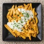 Louisiana Voodoo fries loaded with melted cheese sauce and ranch, garnished with herbs and served as a flavorful comfort food dish.
