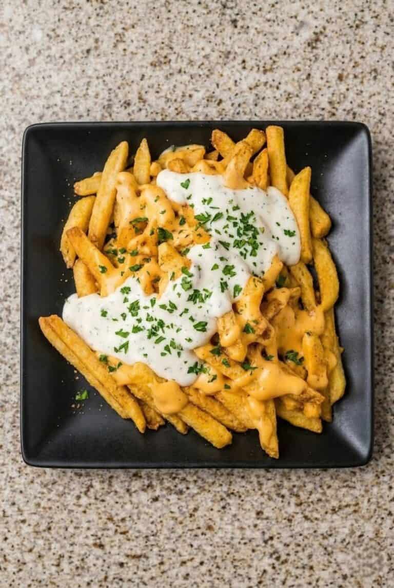 Louisiana Voodoo fries loaded with melted cheese sauce and ranch, garnished with herbs and served as a flavorful comfort food dish.