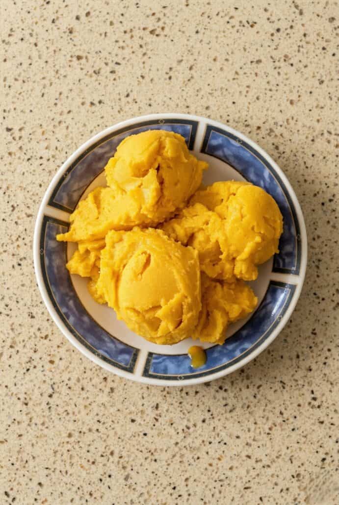 Mango sorbet scoops served in a bowl, showcasing the smooth texture and vibrant color.