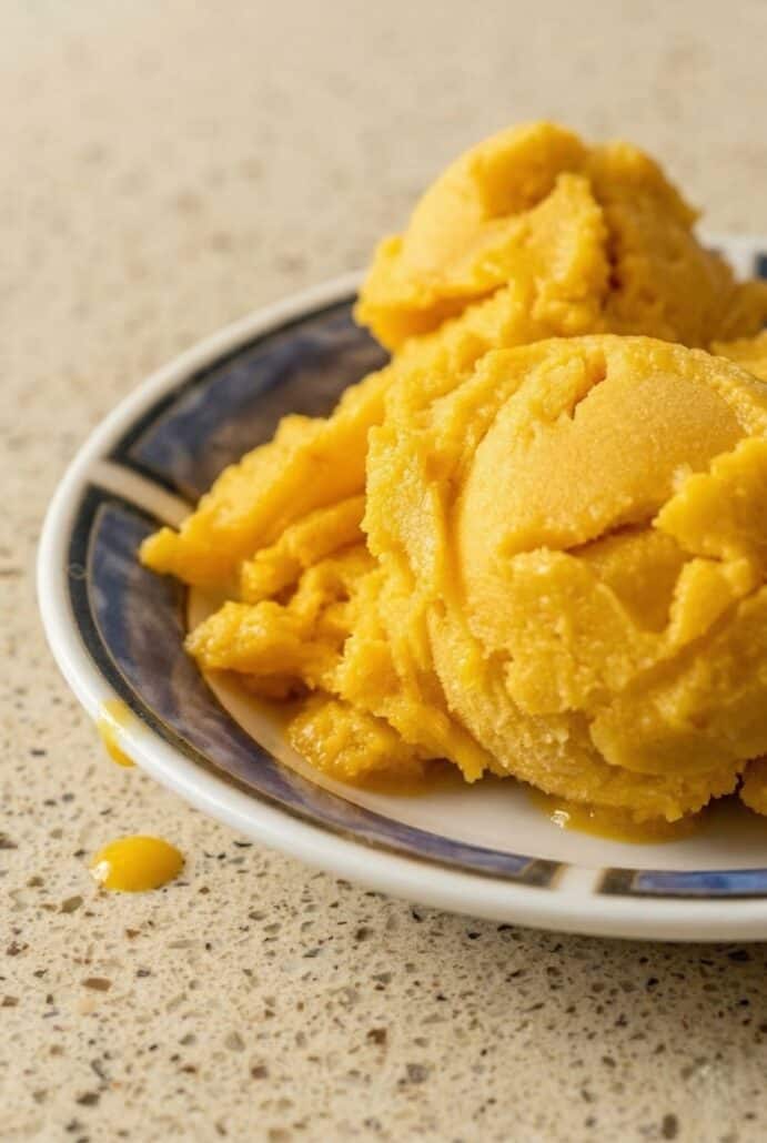Creamy mango sorbet scoops on a plate, highlighting the rich texture and vibrant color.