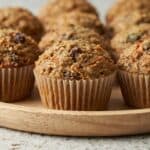 Freshly baked homemade morning glory muffins with carrots, raisins, and nuts on a wooden board.