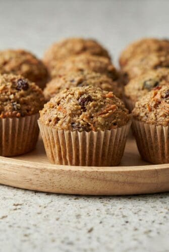 Freshly baked homemade morning glory muffins with carrots, raisins, and nuts on a wooden board.
