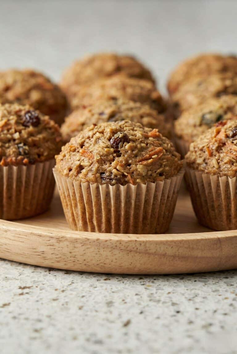 Freshly baked homemade morning glory muffins with carrots, raisins, and nuts on a wooden board.