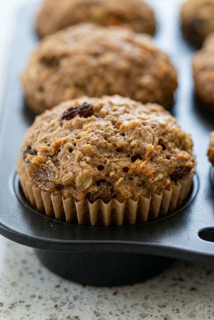 Close-up of a freshly baked morning glory muffin with raisins and shredded carrots in a muffin tin.