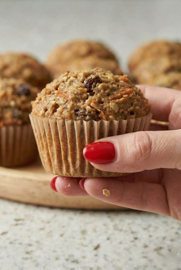 Hand holding a freshly baked morning glory muffin with raisins and carrots, showing the moist texture.