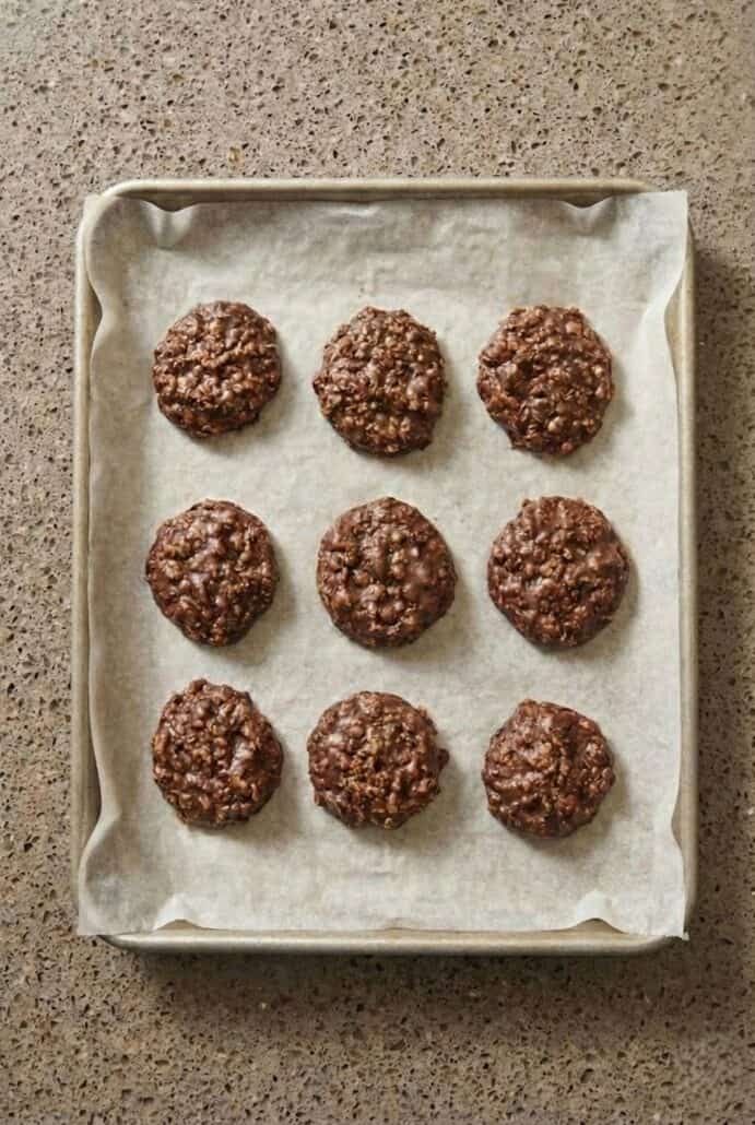 No-bake chocolate oatmeal cookie mixture dropped in rounds on a parchment-lined baking sheet.