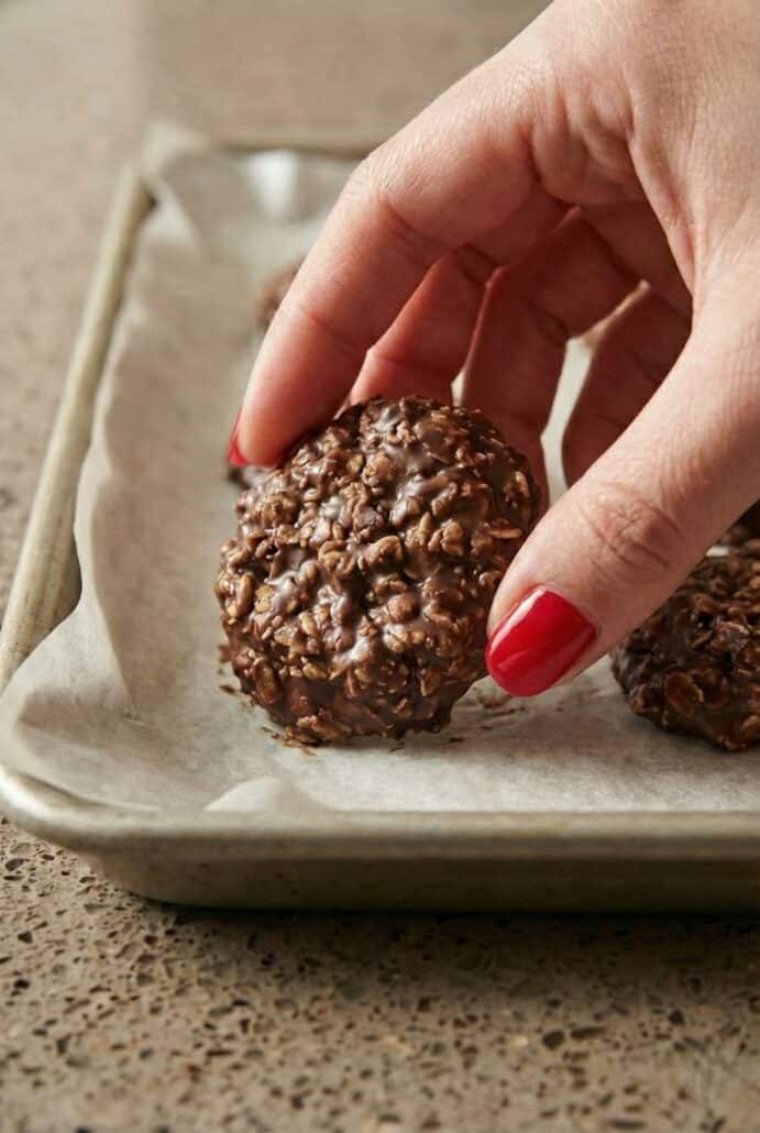 Hand holding a homemade no-bake chocolate oatmeal cookie over a tray, showing the soft chewy texture of this easy chocolate peanut butter oat cookie.