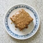 Square slice of peanut butter sheet cake with creamy peanut butter frosting served on a decorative plate.