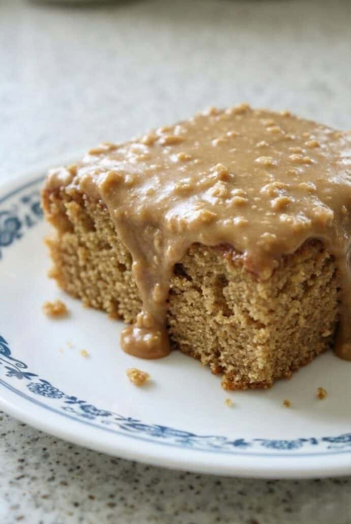 Close-up of peanut butter sheet cake slice with thick, creamy frosting dripping down the sides, showing the moist texture.